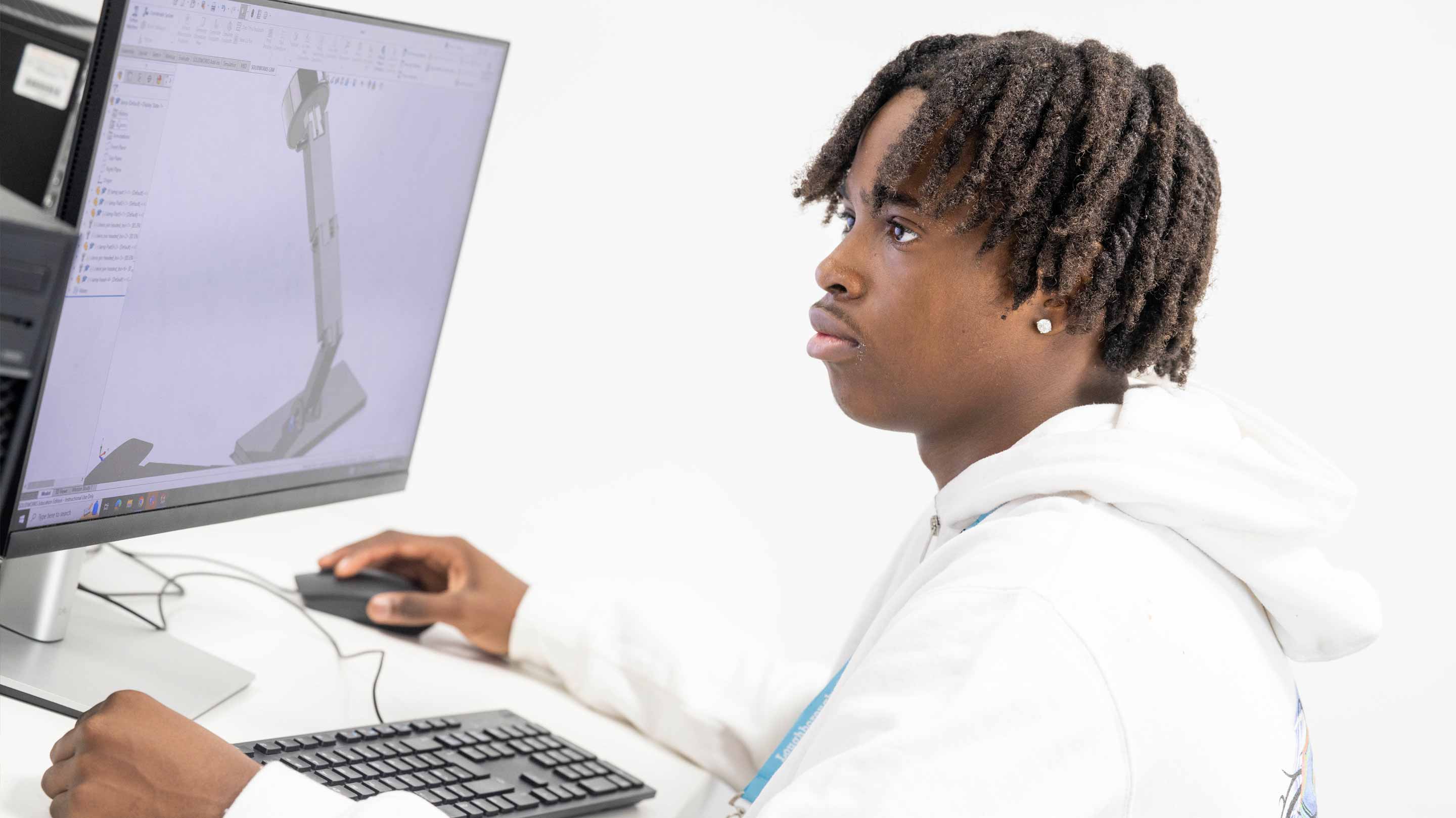 Engineering student sitting at a desk using a computer to creare a 3D CAD model