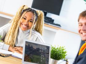 A female student and male teacher sit at a desk facing the camera smiling