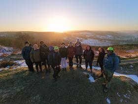 A group of walkers on a hill in the Peak District. There is snow around them and the sun is rising behind them