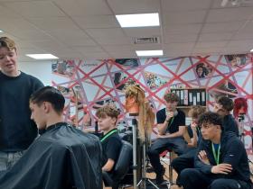 Alumna Alice demonstrates a haircut in front of students in a salon