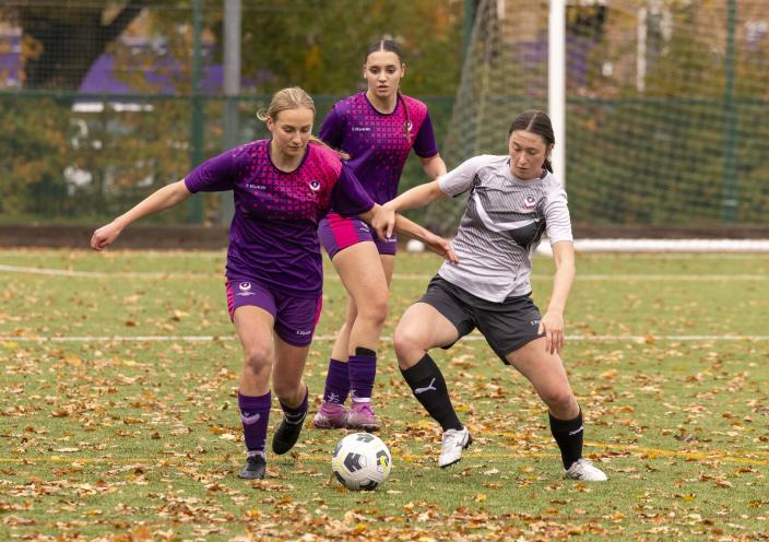 A group of girls playing football on a grass pitch