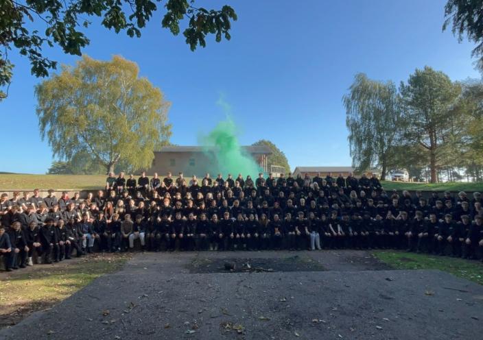 A group photo of the staff, students, and volunteers at the Walesby trip. In the back are trees and a green smoke flare