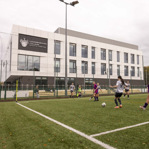 Exterior of the Sports Centre in the background, with students playing football on a pitch in the foreground