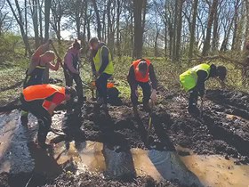 A groups of student outside in high vis clothing digging the ground in a local wood, working on an environmental project