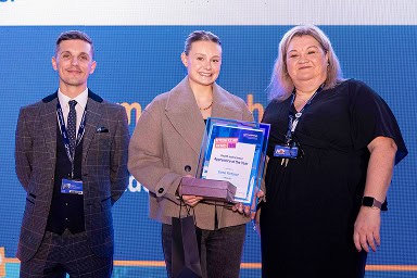 Jonny Watkin, Stephenson Principle, and Jenny Dryden, Stephenson Assistant Principal, standing on stage with Esme Fletcher who won Health and Science Apprentice of the Year 2026