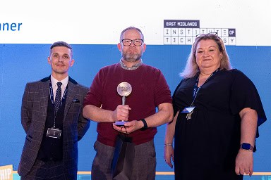 Jonny Watkin, Stephenson Principle, and Jenny Dryden, Stephenson Assistant Principal, standing on stage with Roy Dowell, Druck Quality Manager, accepting the award for Druck after winning Employer of the Year 2026
