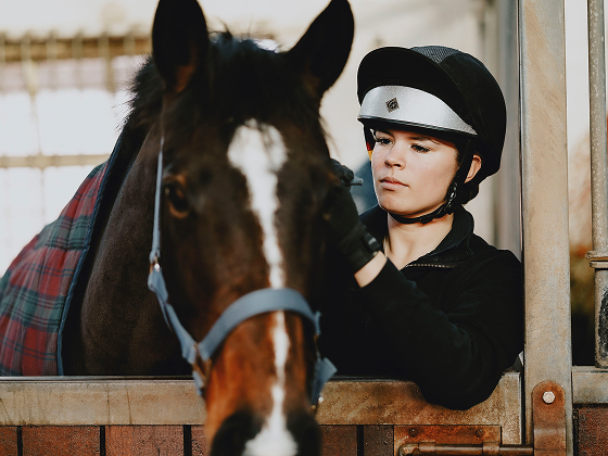 Person wearing a riding helmet holding a horse's bridle