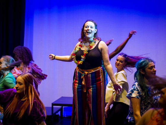 Student standing on a raised platform in the middle of a group,wearing a headset microphone, singing
