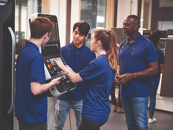 Group of students working at a machine with a supervisor