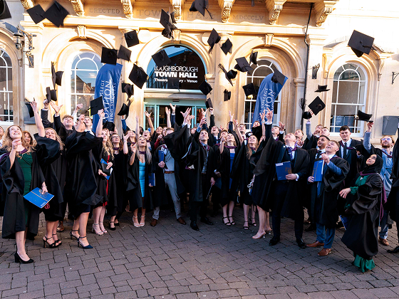 Group of graduating students wearing black gowns, throwing their caps into the air
