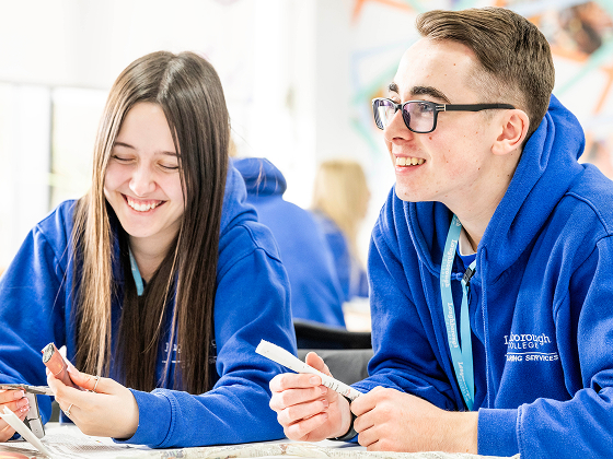 Two students wearing blue hoodies and smiling, sitting at a classroom desk