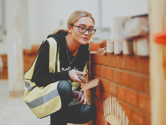 Person wearing a high-vis vest, constructing a red brick wall