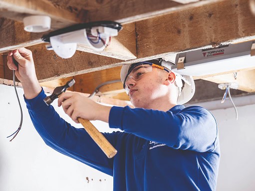 A student in the electrical workshop fitting ceiling lights to a beam