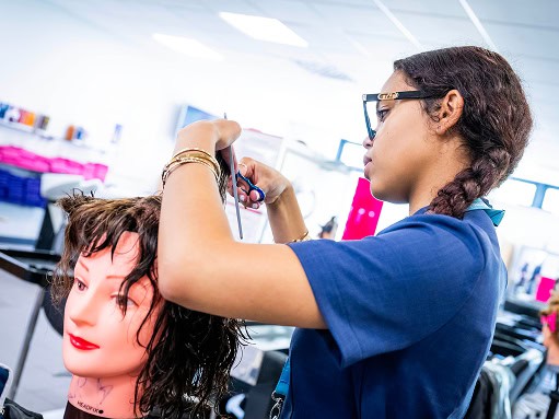 A student in the training salon cutting the hair of a training dummy