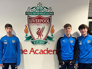 Degree Students at the Liverpool FC Academy standing in front of the LFC club badge