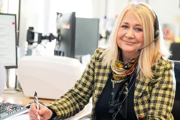 College staff member sitting at the reception desk with a headset on awaiting enquiries