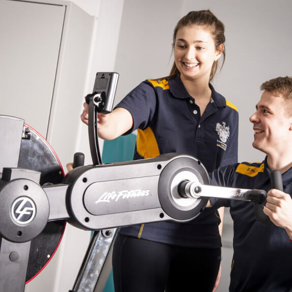 Students at an arm cycle, looking at a monitor
