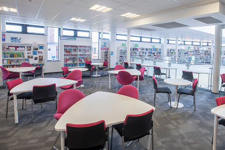 Interior of the library, book shelves around the edge, circular tables with 3 chairs at each table