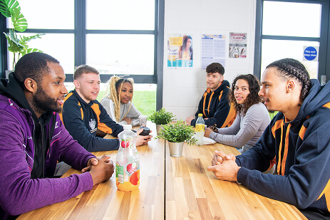 Six students sitting around a table in the Undergraduate Centre common room talking