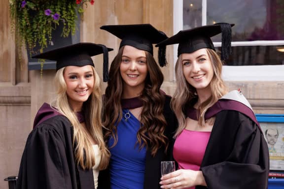 Group of 3 female students standing together in graduation gowns