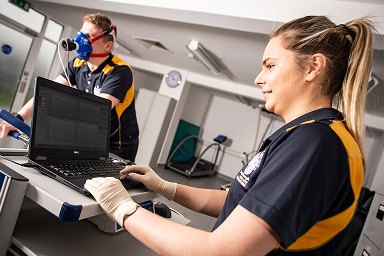 Students in the Sports Lab one on a bike wearing a breathing mask the other examining data on a laptop
