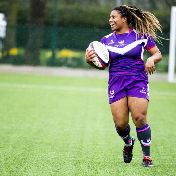 A student running on a pitch, holding a rugby ball
