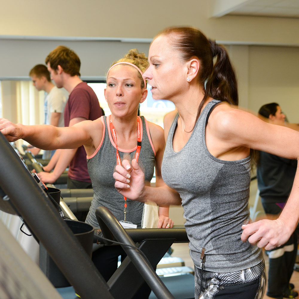 A woman running on a treadmill with a trainer.