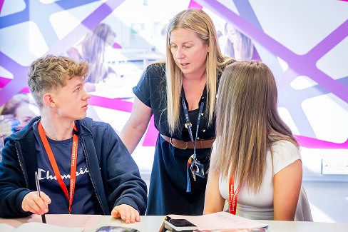 A teacher talking with two students during a lesson answering their questions