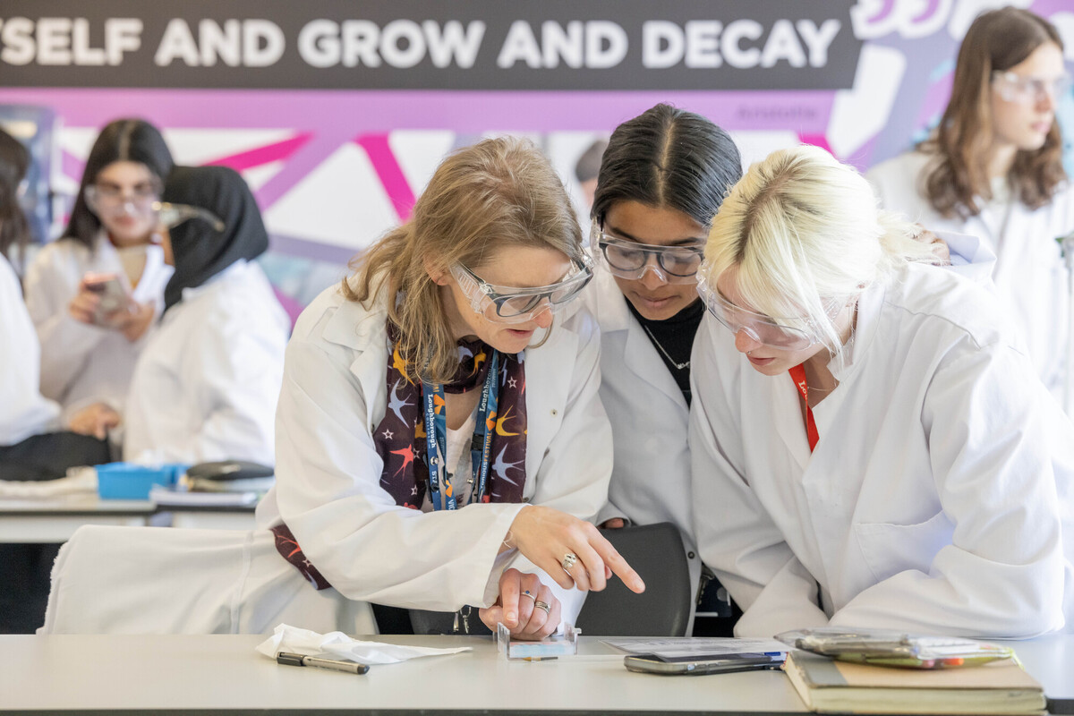 Teacher and students wearing safety goggles, looking at a glass slide