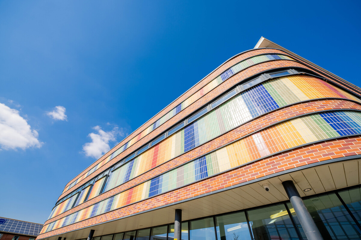 A brick building with multicoloured tiles, viewed from a low angle, against a bright blue sky