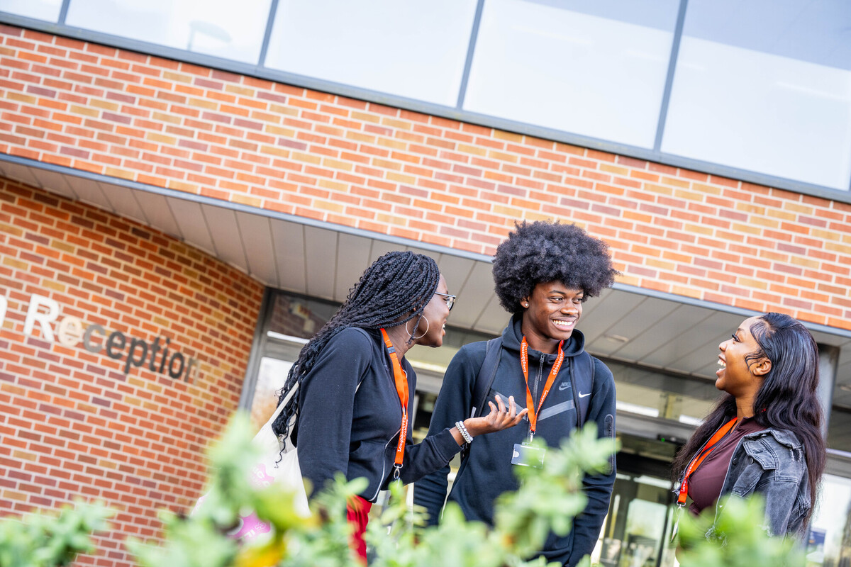 Group of three students talking and smiling in front of a brick building